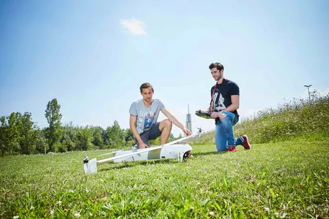 Zwei Studierende arbeiten an einem kleinen Flugzeugmodell im Freien auf einer Wiese. 